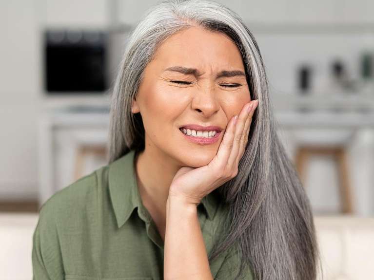A woman holding her cheek, experiencing a toothache from a tooth infection