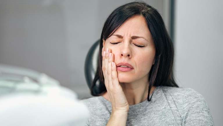 A woman with a toothache in a dentist's chair, highlighting the need for emergency dental care.